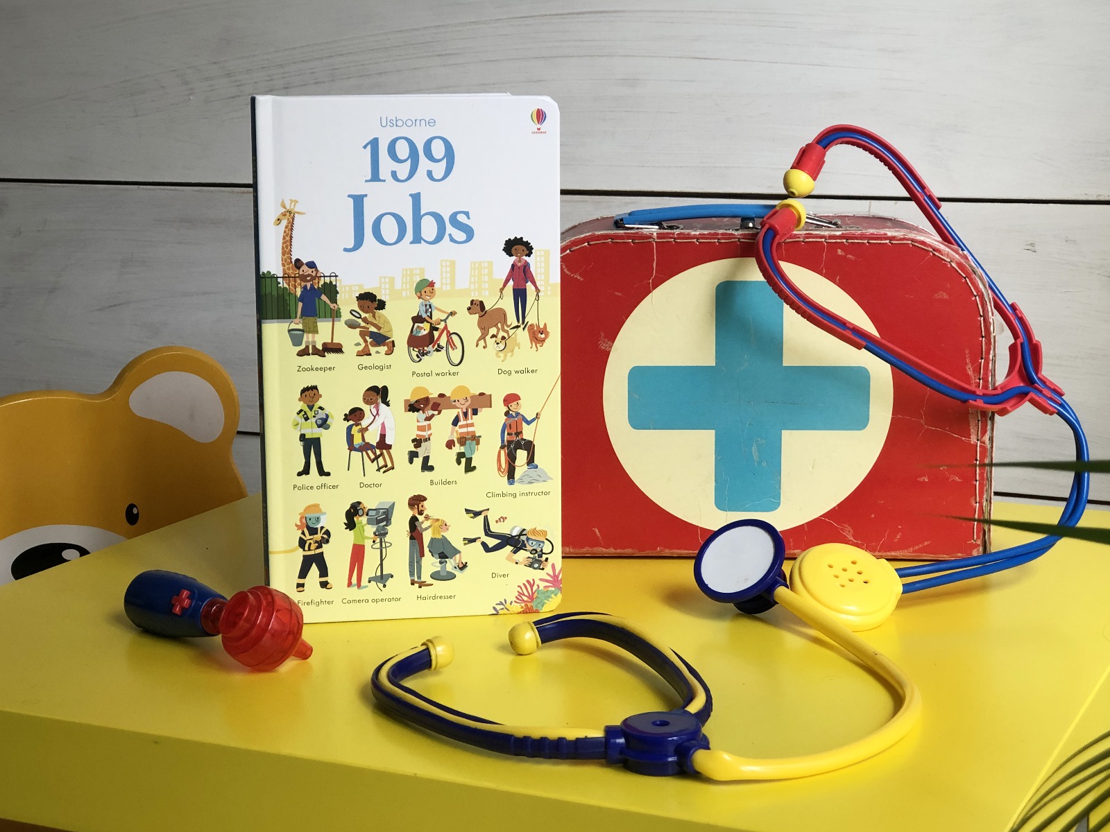 A book standing next to a toy first aid kit and a toy stethoscope. 