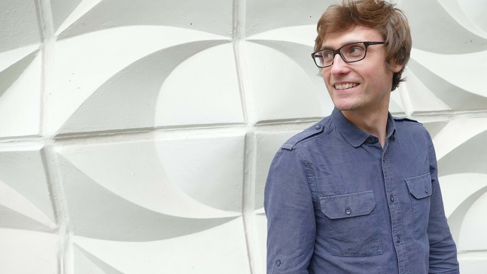 A person wearing black glasses and a blue shirt staring off to the left and smiling.