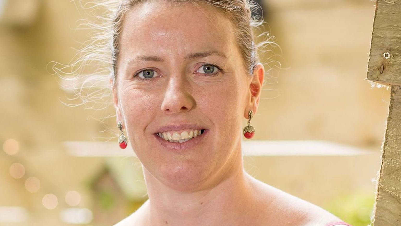 A person smiling at the camera wearing a white top with red stitching.