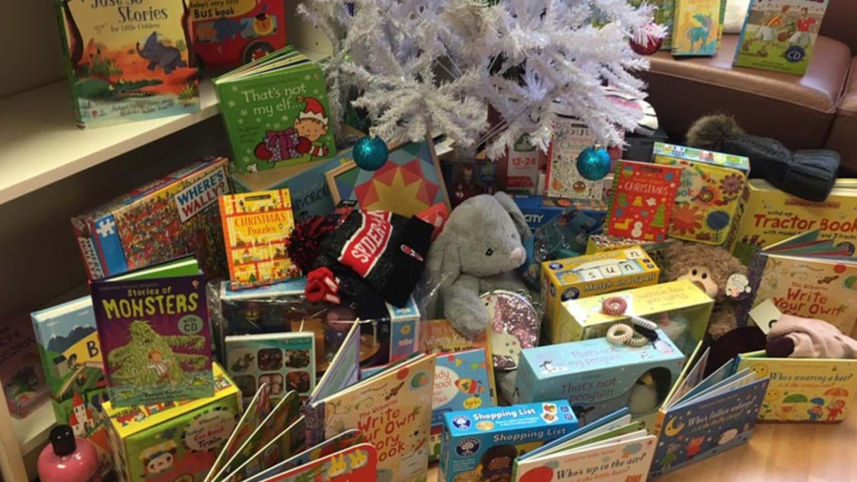 Books and toys placed under a white Christmas tree in an office.