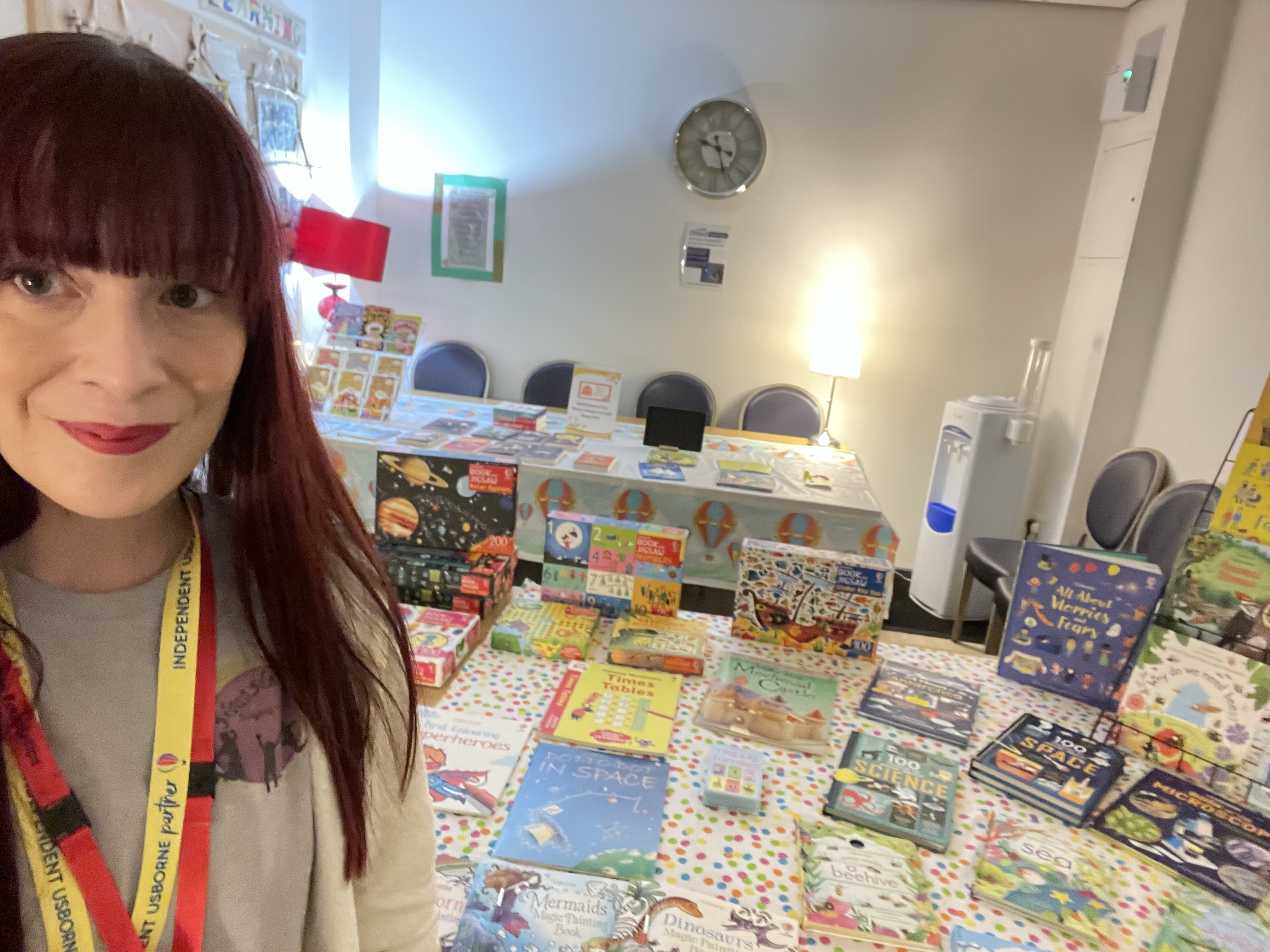 Rows of books lined up on a table. A woman is smiling and standing next to the books.
