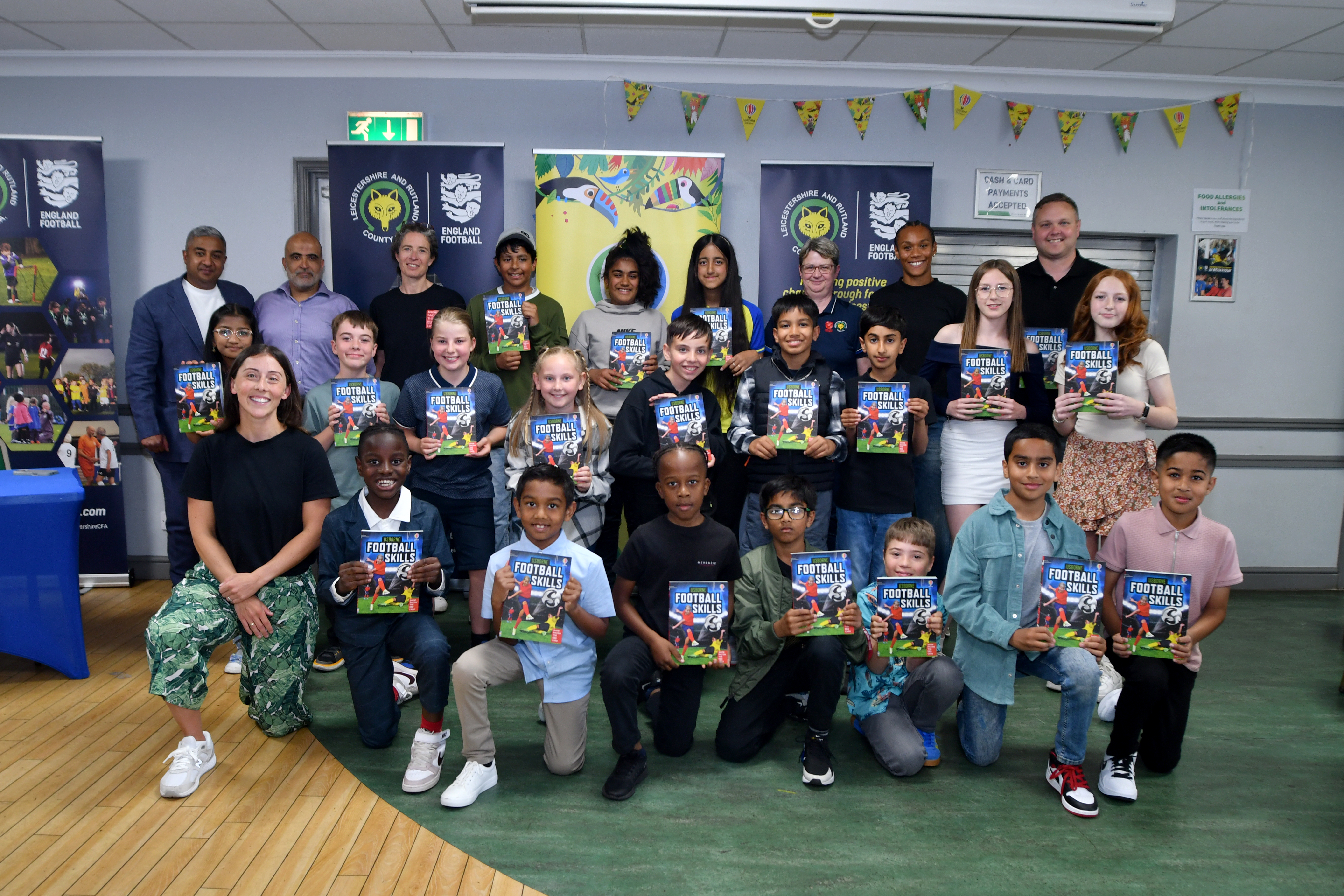 A group of children and adults standing together holding a copy of a new book release called Football Skills.