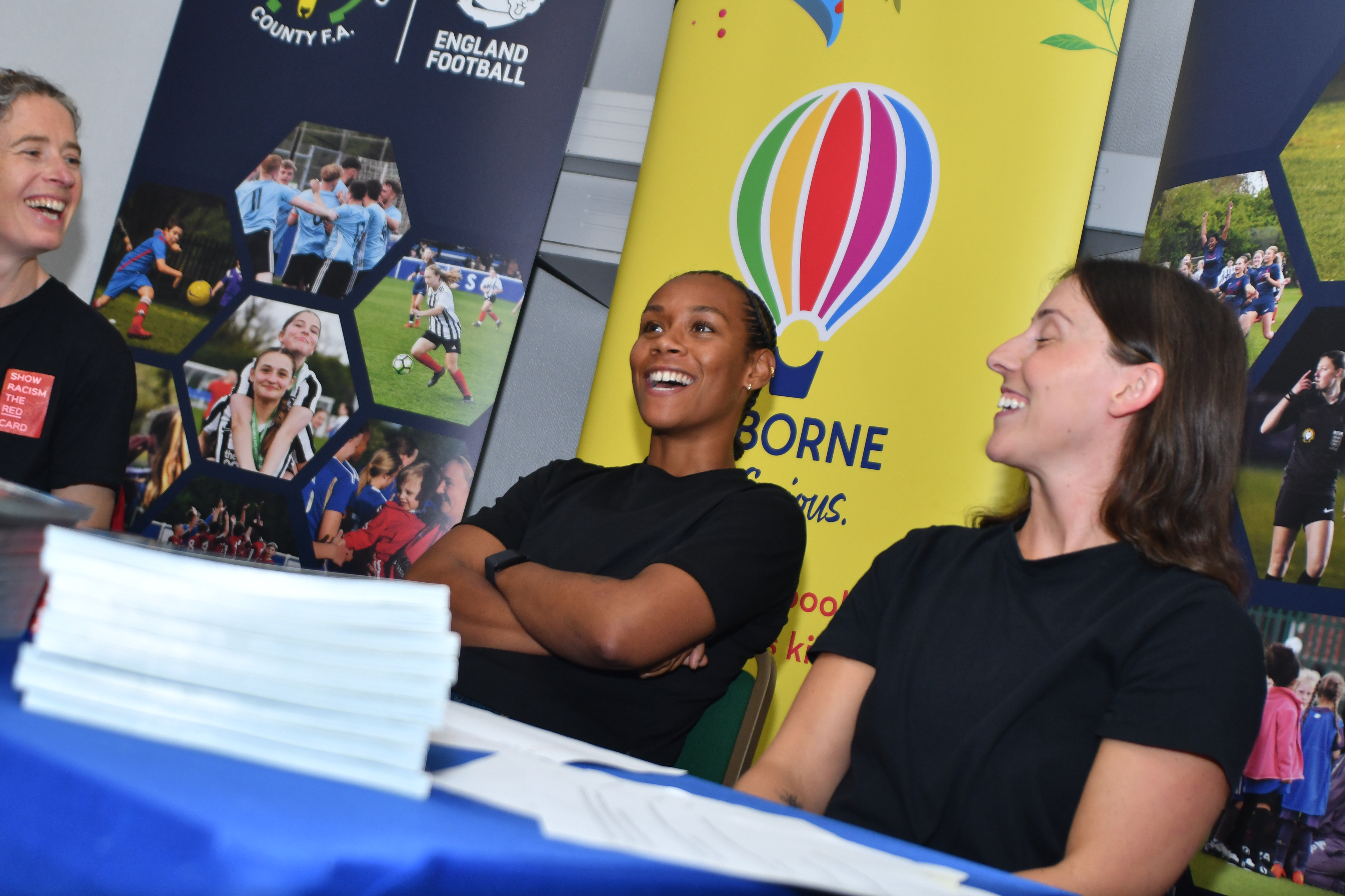 Three people exchange laughter at a conference table filled with books.