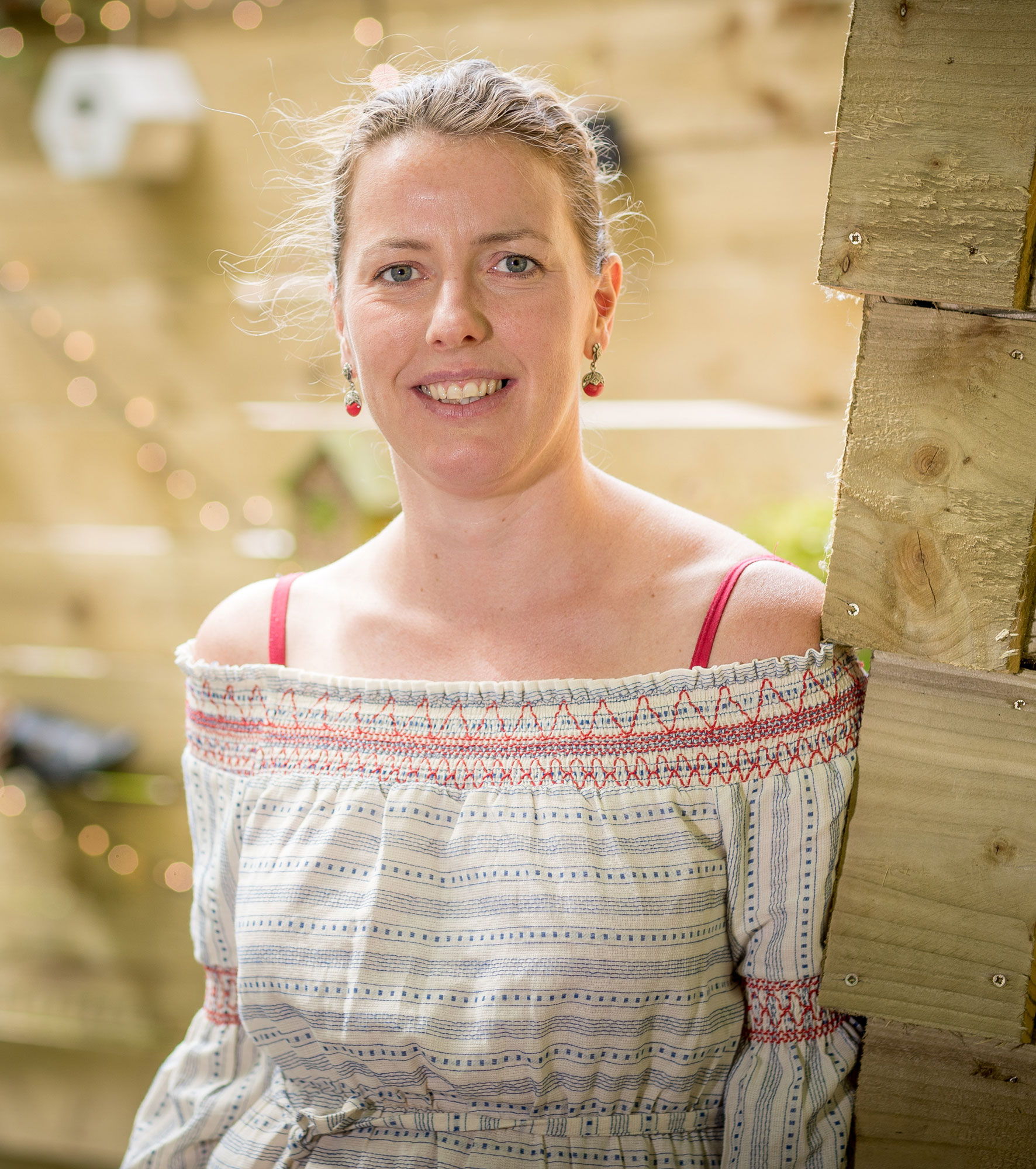 A person smiling at the camera wearing a white top with red stitching.