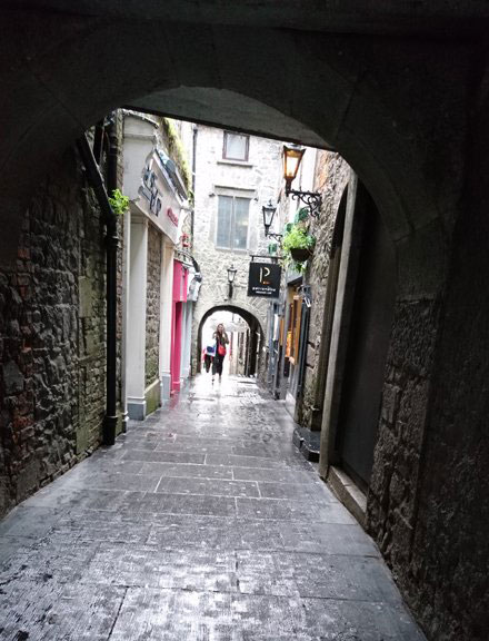 A narrow street paved in stone with light rain.