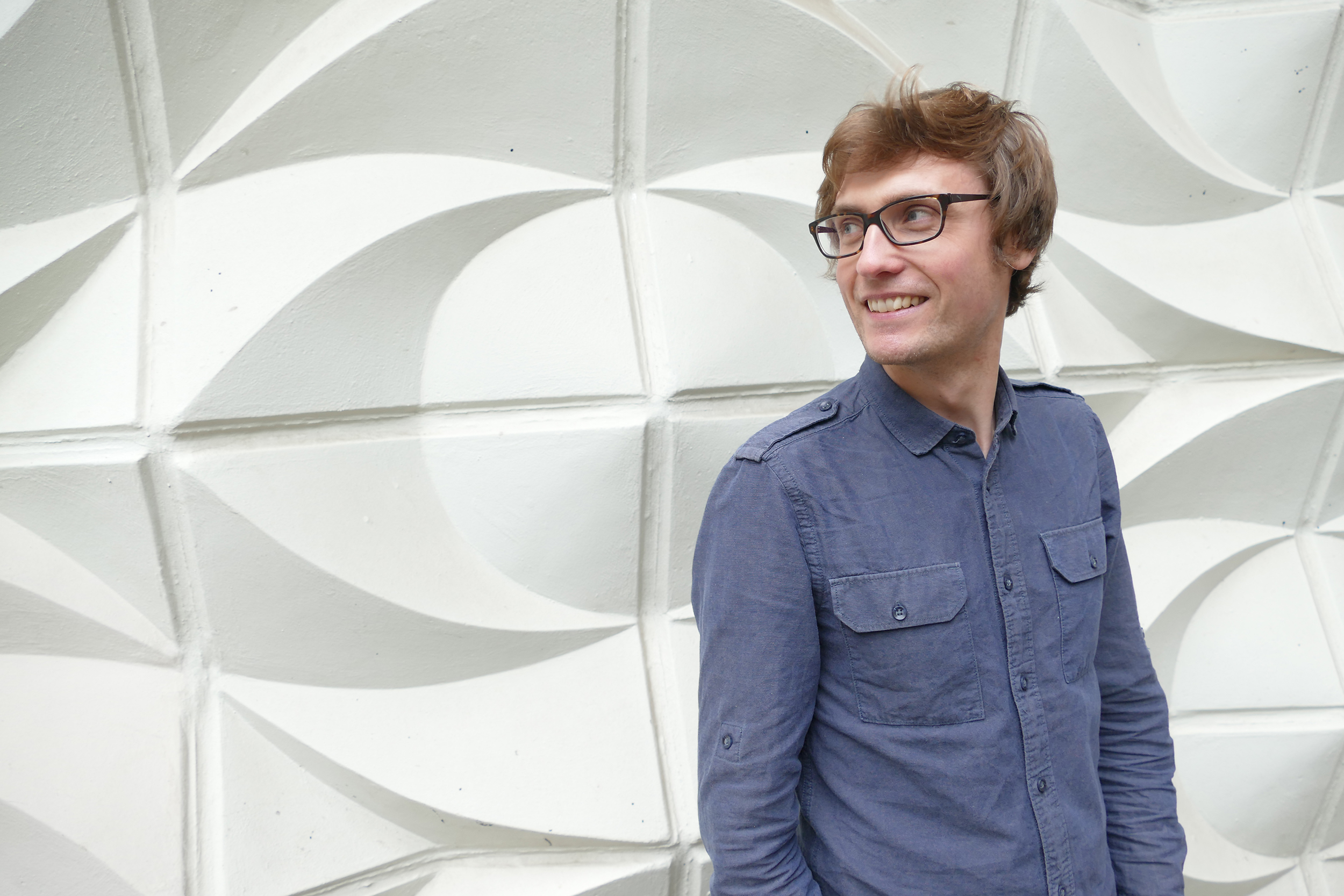 A person wearing black glasses and a blue shirt staring off to the left and smiling.