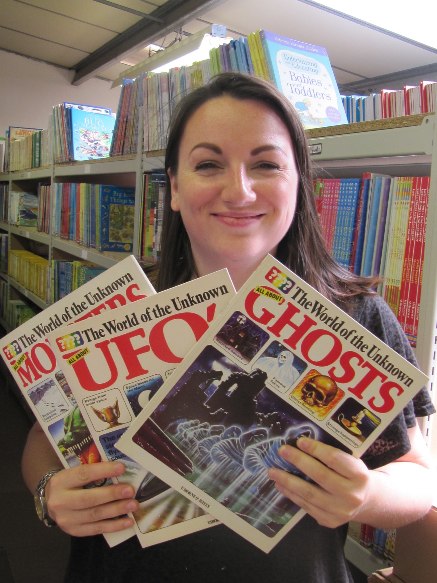 A person holding books about UFOs Ghosts and Monsters.